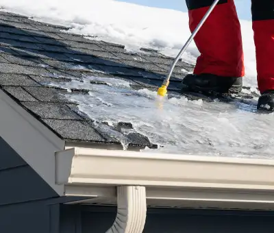 Ice dam removal technician using a steam wand to melt thick ice buildup on a residential roof in Green Bay, WI