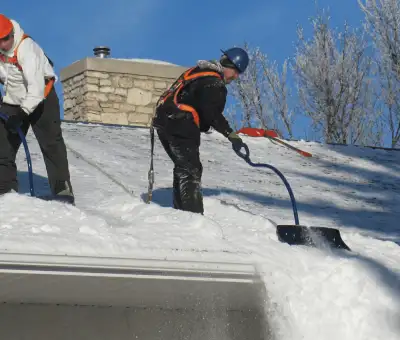 Professional technicians performing roof snow removal with safety harnesses and shovels in Green Bay, WI